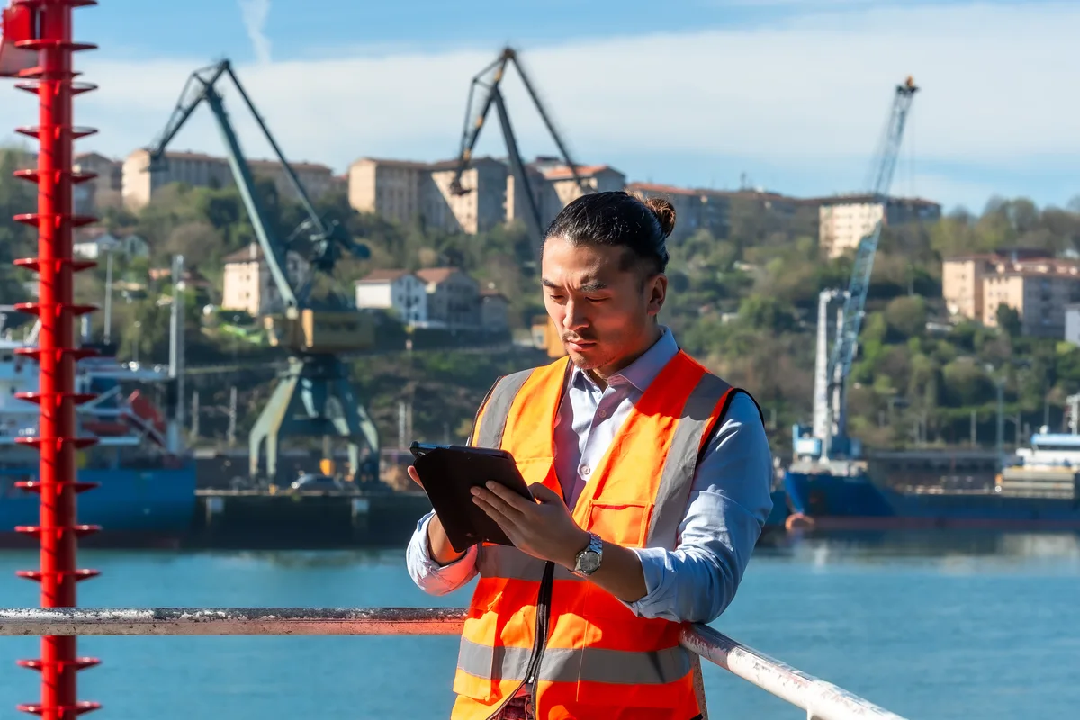 Port worker using a tablet beside dockside cranes